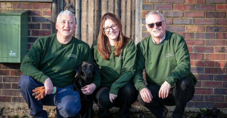 A picture of three people kneeling accompanied by a black Labrador